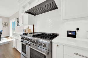 Kitchen featuring double oven range, white cabinetry, light stone counters, light wood-type flooring, and decorative backsplash