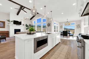 Kitchen featuring white cabinetry, range hood, a fireplace, stainless steel appliances, and vaulted ceiling