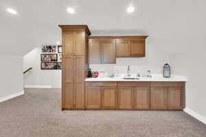 Bar area featuring light countertops, wood finish cabinetry, light colored carpet, lofted ceiling, and recessed lighting