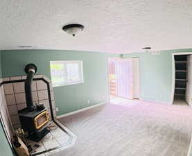 Unfurnished living room featuring a textured ceiling, light colored carpet, a wood stove, and light tile patterned floors