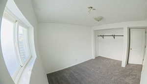 Unfurnished bedroom featuring a textured ceiling, carpet flooring, and a closet