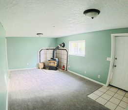 Unfurnished living room with a wood stove, light colored carpet, and a textured ceiling