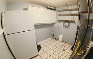 Laundry room with a textured ceiling, hookup for an electric dryer, light tile patterned flooring, and cabinet space