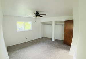 Unfurnished bedroom with two closets, carpet floors, and a ceiling fan