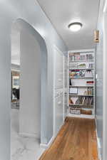 Hallway with arched walkways, a textured ceiling, and light wood-type flooring