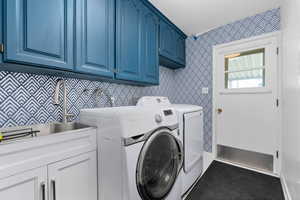 Laundry room featuring wallpapered walls, cabinet space, and washing machine and dryer