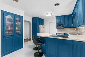 Kitchen featuring light countertops, arched walkways, a breakfast bar, and blue cabinetry