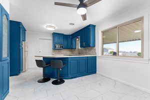 Kitchen featuring blue cabinetry, light countertops, a peninsula, a breakfast bar area, and ceiling fan