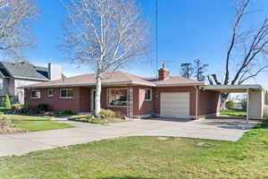 Ranch-style home featuring an attached garage, a chimney, a front lawn, and concrete driveway