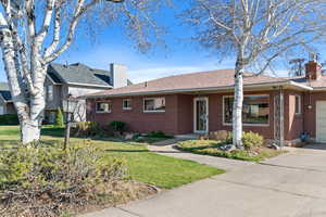 Ranch-style home featuring a chimney, a front lawn, brick siding, an attached garage, and concrete driveway