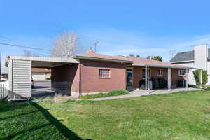 Back of house featuring a yard, an attached carport, brick siding, and a patio