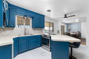 Kitchen with ceiling fan, blue cabinets, light countertops, and light marble finish floors