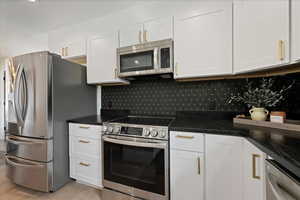 Kitchen featuring stainless steel appliances, white cabinetry, dark stone countertops, and light wood-style floors