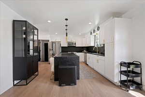 Kitchen with stainless steel appliances, white cabinets, light wood-style floors, tasteful backsplash, and a center island