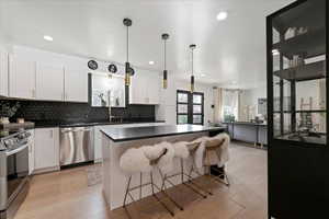 Kitchen featuring a kitchen island, a kitchen breakfast bar, white cabinets, backsplash, and stainless steel appliances