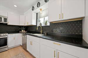 Kitchen featuring white cabinets, stainless steel appliances, light wood-style flooring, recessed lighting, and backsplash