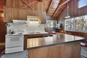 Kitchen featuring white electric range oven, a high wooden beamed ceiling, wooden walls, hanging light fixtures, and black microwave