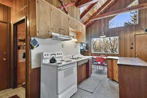 Kitchen featuring wooden walls, white electric range oven, a high wood beamed ceiling, light countertops, and wood finish cabinetry