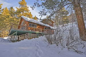 View of snowy exterior featuring a wooden deck and faux log siding