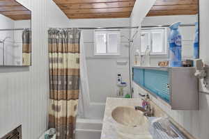Bathroom with wooden ceiling, vanity, shower / tub combo, wood walls, and healthy amount of natural light