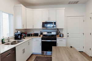 Kitchen with quartz counters, stainless steel appliances, light wood-style floors, and white cabinets
