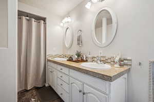 Bathroom featuring double vanity, backsplash, and curtained shower