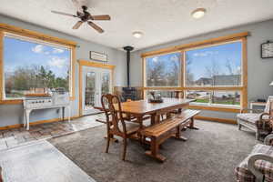 Dining room featuring a wood stove, a ceiling fan, a textured ceiling, and french doors