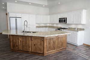 Kitchen with light stone countertops, a large island with sink, stainless steel appliances, a high ceiling, and recessed lighting
