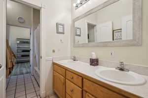 Full bath with double vanity, a shower with shower curtain, light tile patterned floors, and a walk in closet