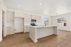 Kitchen featuring light wood-style floors, hanging lights, stainless steel appliances, and a kitchen island with sink