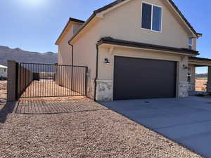 View of front of house with stone siding, a gate, driveway, and stucco siding