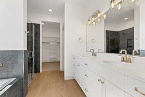 Full bath with a bath, double vanity, a spacious closet, light wood-style floors, and a shower stall