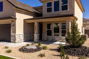 View of front facade with a porch, stone siding, stucco siding, and a garage