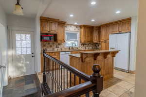 Kitchen featuring wood finish cabinets, white refrigerator with ice dispenser, light stone countertops, a breakfast bar, and a center island