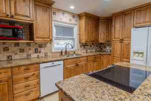 Kitchen with light stone countertops, black appliances, wood finish cabinetry, decorative backsplash, and recessed lighting