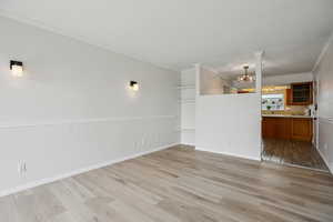 Unfurnished living room featuring crown molding, light wood finished floors, built in features, and hanging lights