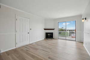 Unfurnished living room with light wood-style flooring, crown molding, and a glass covered fireplace