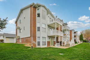 Back of property with a lawn, a patio area, brick siding, and a balcony