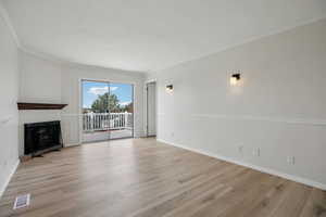 Unfurnished living room featuring a glass covered fireplace, light wood-style flooring, and crown molding