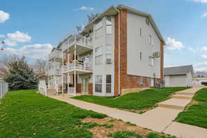 View of side of property featuring brick siding, a lawn, and a balcony