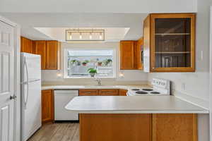 Kitchen with wood finish cabinets, a peninsula, white appliances, light countertops, and wood tiled floors