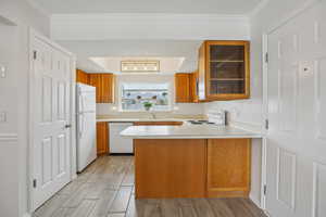 Kitchen with a peninsula, wood finish cabinetry, light countertops, wood tiled floors, and white appliances