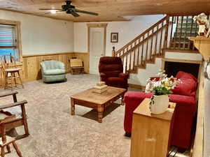 Carpeted living room featuring wooden walls, wainscoting, and a ceiling fan