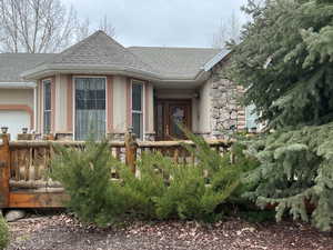 Doorway to property with a shingled roof, stone siding, stucco siding, a wooden deck, and a garage