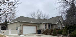 View of front of house featuring stone siding, a garage, and roof with shingles