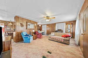Carpeted living area with wooden walls, ceiling fan, and a textured ceiling