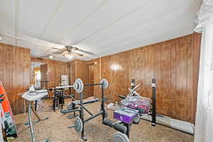 Exercise area with wooden walls, a ceiling fan, and light colored carpet