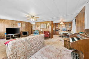 Living area with wooden walls, light carpet, a desk, and ceiling fan