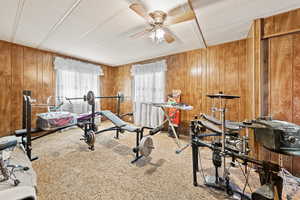 Exercise area with a ceiling fan, carpet flooring, and wood walls