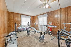 Exercise room featuring carpet flooring, wood walls, a ceiling fan, and a textured ceiling